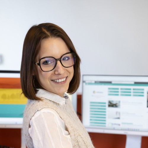Portrait d'une jeune femme souriante assise à son bureau devant ses 2 écrans. Photographie réalisée pour la communication "Marque Employeur" du réseau Cerfrance. | Philippe DUREUIL Photographie