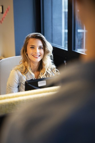 Photographe Corporate. Jeune femme souriante à son poste de travail dans l'entreprise, elle regarde dans l'objectif. | Philippe DUREUIL Photographie