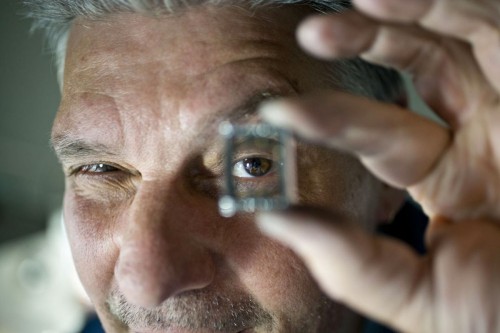 Photographie industrielle d'un horloger regardant au travers d'un boitier de montre en fabrication. Reportage photo industriel réalisé pour la manufacture horlogère Jaeger-LeCoultre. | Philippe DUREUIL Photographie