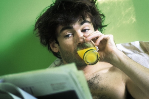 Homme au réveil dans sont lit qui boit un jus d'orange et lit le journal | Philippe DUREUIL Photographie