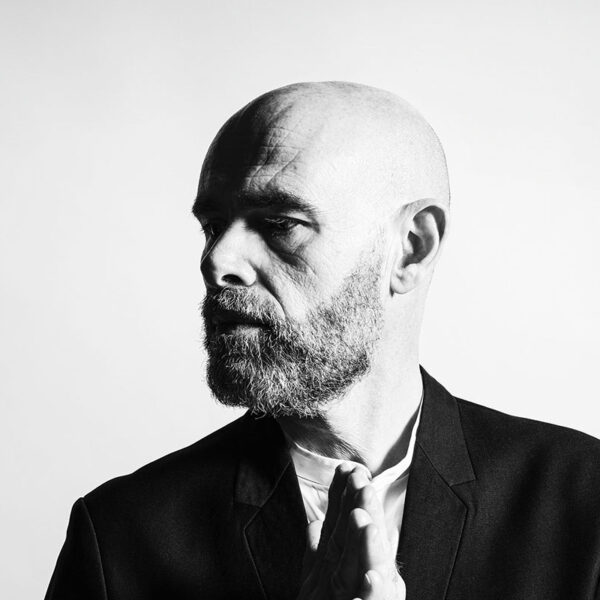 Portrait artistique en noir et blanc d'un homme mûr avec barbe, les mains jointes dans une posture de réflexion sur fond blanc.